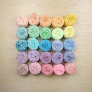 May include: A collection of twenty-five small, round yarn balls arranged in a five-by-five grid. The yarn balls display a gradient of pastel colors, including shades of pink, peach, yellow, green, blue, purple, and lavender, with a soft texture.