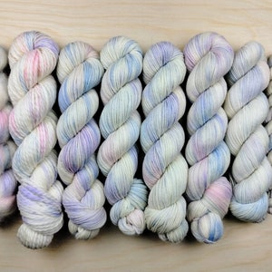May include: Eight skeins of yarn in a variety of pastel colors, including pink, blue, and purple. The yarn is arranged in a row, with the ends of each skein overlapping.