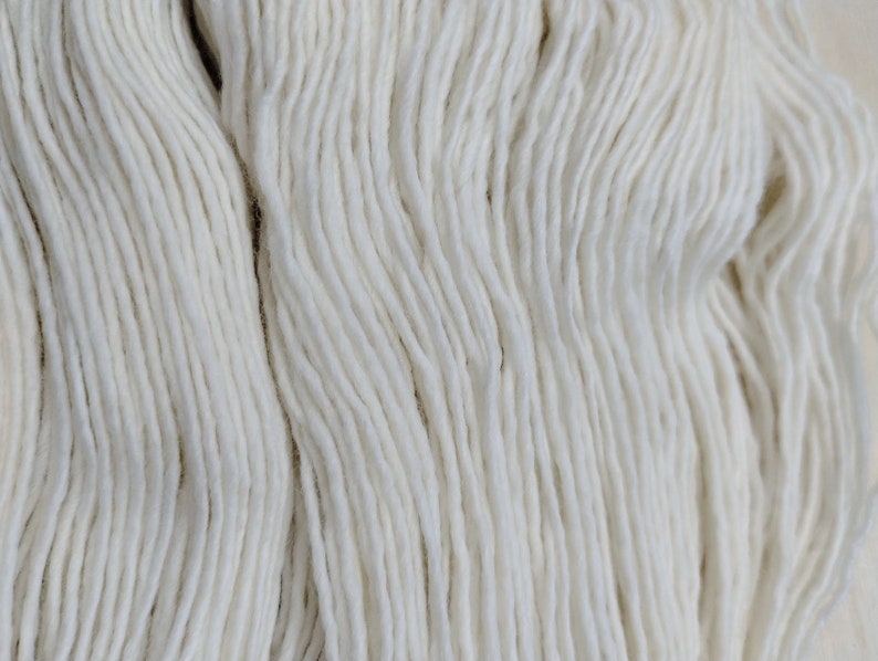 May include: A close-up of a skein of white yarn. The yarn is soft and fluffy, and it is perfect for knitting or crocheting.