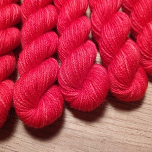 May include: Close-up of six skeins of bright red yarn, twisted and arranged in a heart shape. The yarn is soft and fluffy, perfect for knitting or crocheting.