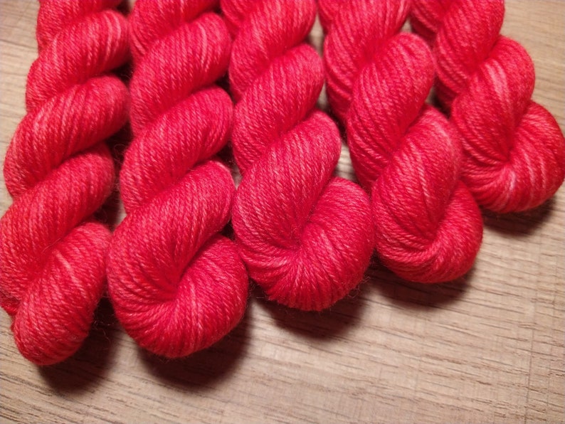 May include: Close-up of six skeins of bright red yarn, twisted and arranged in a heart shape. The yarn is soft and fluffy, perfect for knitting or crocheting.