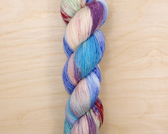 May include: A skein of colorful yarn in shades of blue, purple, red, and cream. The yarn is twisted and appears soft, with a gradient effect. The yarn is likely used for knitting or crocheting projects.