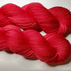 May include: A skein of bright red yarn, twisted and folded, showing the soft texture of the fibers.