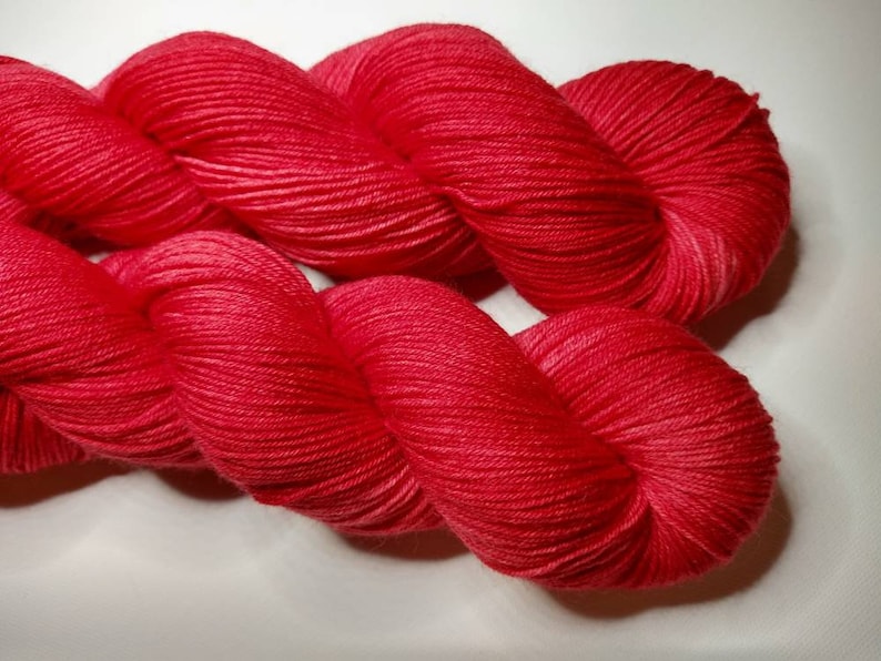 May include: A skein of bright red yarn, twisted and folded, showing the soft texture of the fibers.