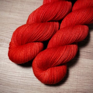 May include: A skein of bright red yarn, wound into a loose coil. The yarn is soft and fluffy, and the color is vibrant and eye-catching.