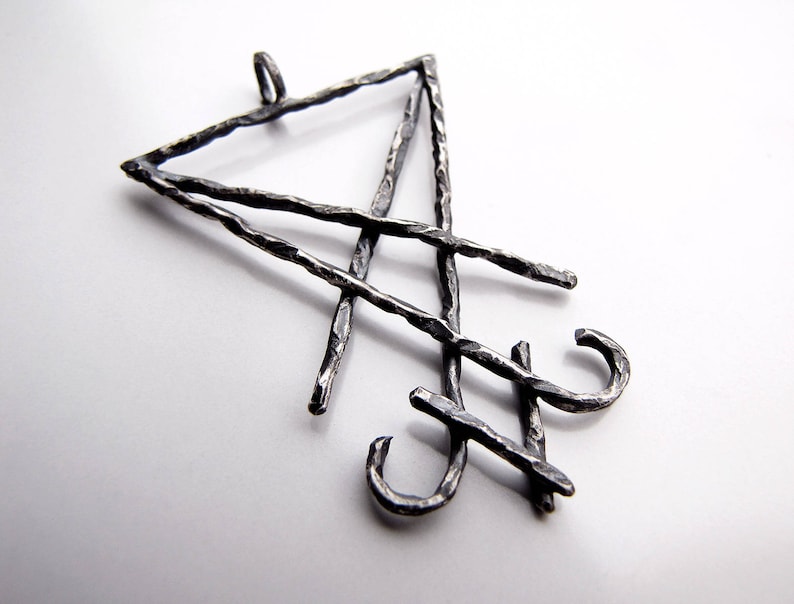 May include: A silver-toned pendant with a geometric design. The pendant features a triangle and intersecting lines with a textured, hammered appearance. The design includes two curved hooks. The pendant is displayed against a white background.