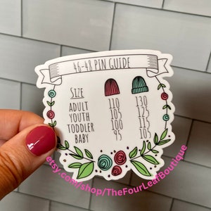 May include: A white sticker with a floral border and a chart for 46-48 pin knitting needles. The chart lists the size of the knitter (adult, youth, toddler, baby) and the corresponding needle size in inches. The text "etsy.com/shop/TheFourLeafBoutique" is at the bottom of the sticker.