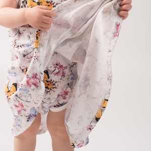 Puede incluir: Un body blanco para bebé con estampado floral y de mariposas. El body tiene mangas cortas y cuello redondo.