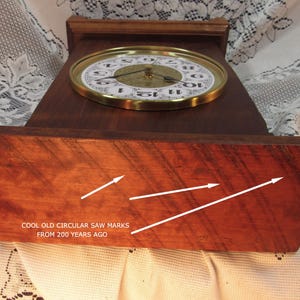 May include: A vintage wooden clock with a round face and gold-colored trim. The clock face displays black numerals on a white background. The wooden base has visible circular saw marks and the text "COOL OLD CIRCULAR SAW MARKS FROM 200 YEARS AGO."