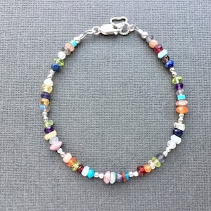 May include: A silver bracelet with a variety of colorful gemstones, including red, orange, yellow, green, blue, purple, and pink.