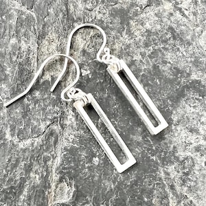 May include: A pair of silver earrings with a simple rectangular design. The earrings are made of thin metal and have a delicate, minimalist style.