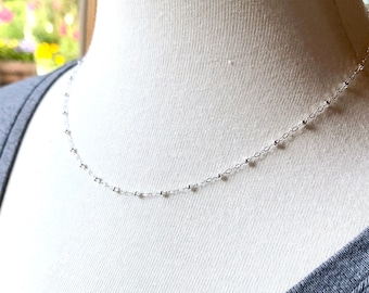 May include: A delicate silver chain necklace with small round beads. The necklace is on a white mannequin.