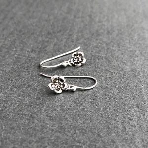 K&ouml;nnte beinhalten: Ein Paar silberne Ohrringe mit Blumenform und schlichtem Design.