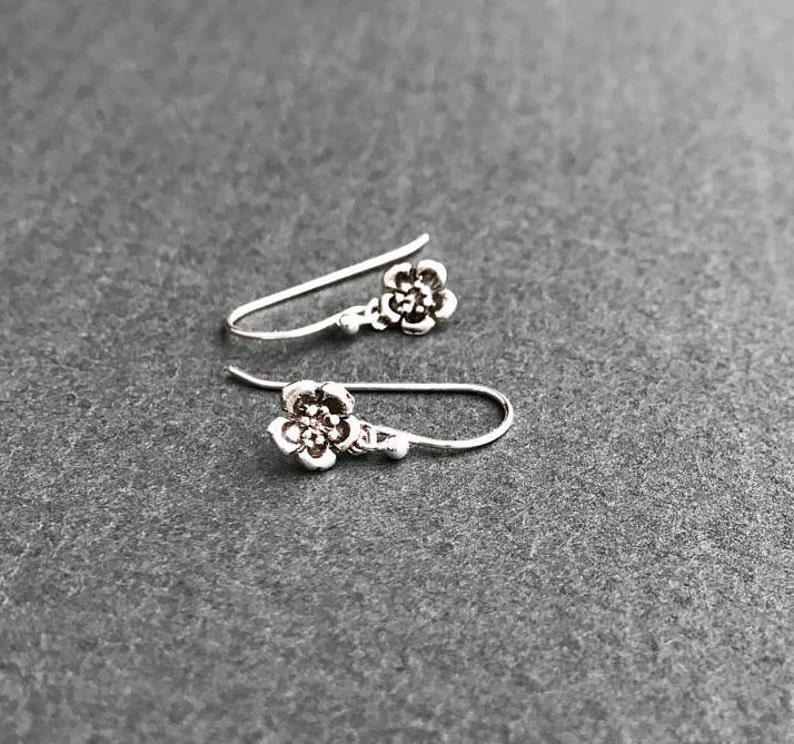 K&ouml;nnte beinhalten: Ein Paar silberne Ohrringe mit Blumenform und schlichtem Design.
