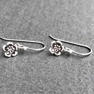 K&ouml;nnte beinhalten: Ein Paar silberne Ohrringe mit Blumen-Anh&auml;ngern. Die Ohrringe bestehen aus einem zarten Silberdraht und haben einen kleinen, detaillierten Blumenanh&auml;nger.