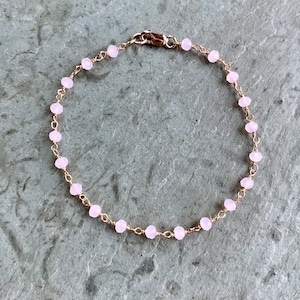Pode incluir: Um delicado bracelete de corrente de ouro rosa com pequenas contas rosa claro. O bracelete tem um fecho de lagosta.
