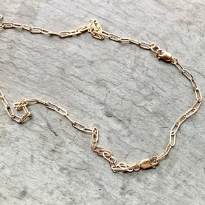 May include: A gold chain necklace with a lobster clasp closure. The chain is made of small, oval-shaped links.
