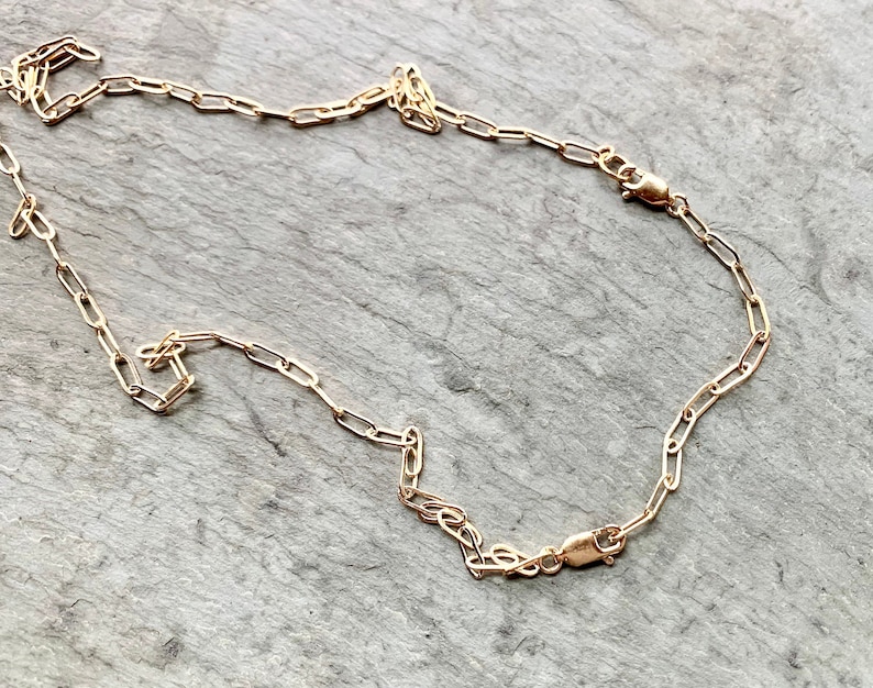 May include: A gold chain necklace with a lobster clasp closure. The chain is made of small, oval-shaped links.