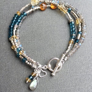 May include: A multi-strand bracelet with silver beads, blue topaz, labradorite, and citrine gemstones. The bracelet has a silver toggle clasp and a heart charm.
