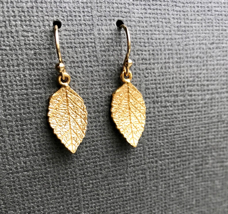 May include: A pair of gold leaf earrings with a delicate, textured design. The earrings are made of metal and have a simple, elegant style.