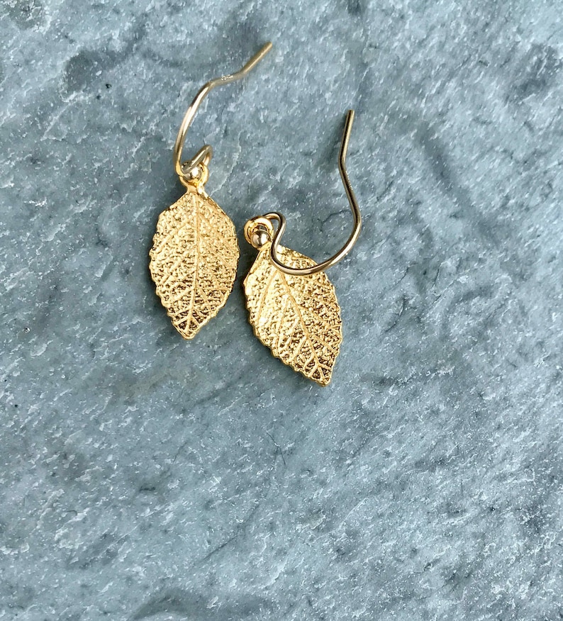 May include: A pair of gold leaf earrings with a delicate design. The earrings are made of metal and have a simple, elegant style.