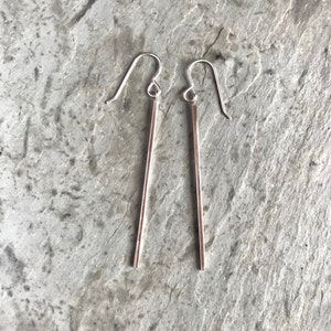 May include: A pair of silver dangle earrings with thin, straight bars hanging from the hooks.