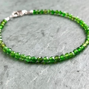 Op de afbeelding: Een groene edelsteen armband met een zilveren sluiting. De armband is gemaakt van kleine, ronde kralen die in grootte aflopen, met de grotere kralen aan de onderkant. De kralen zijn een levendige groene kleur en hebben een licht iriserende glans.