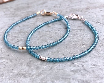 Peut inclure: Deux bracelets délicats faits de minuscules perles de topaze bleue. Un bracelet a un accent doré et l'autre un accent argenté.