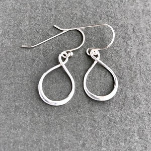 Könnte beinhalten: Ein Paar silberne Ohrringe in Tropfenform mit einem gedrehten Drahtdesign. Die Ohrringe haben einen schlichten, minimalistischen Stil.