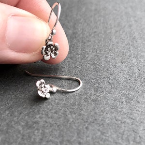 K&ouml;nnte beinhalten: Ein Paar silberne Ohrringe mit Blumen-Anh&auml;ngern. Die Ohrringe bestehen aus einem zarten Silberdraht und haben einen kleinen Blumen-Anh&auml;nger.