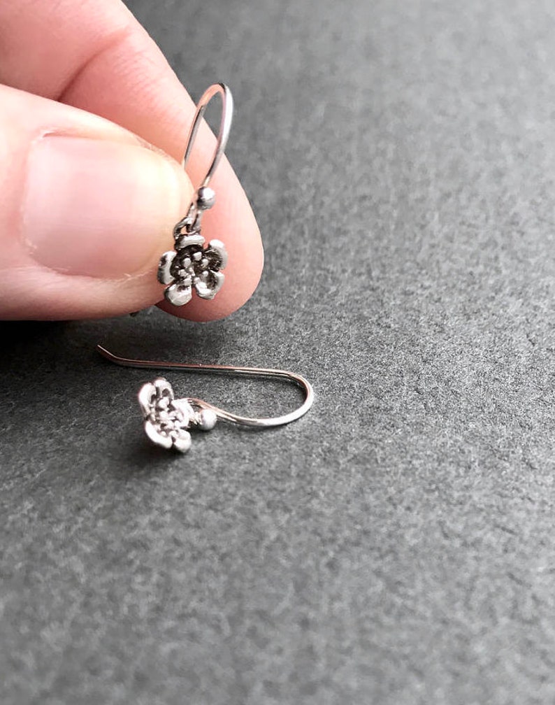 K&ouml;nnte beinhalten: Ein Paar silberne Ohrringe mit Blumen-Anh&auml;ngern. Die Ohrringe bestehen aus einem zarten Silberdraht und haben einen kleinen Blumen-Anh&auml;nger.