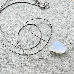 May include: A silver chain necklace with a white moonstone pendant. The moonstone is a natural, irregular shape and has a pearly sheen.