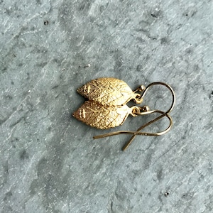 May include: A pair of gold leaf earrings with a delicate design. The earrings are made of gold-plated metal and have a simple, elegant look.