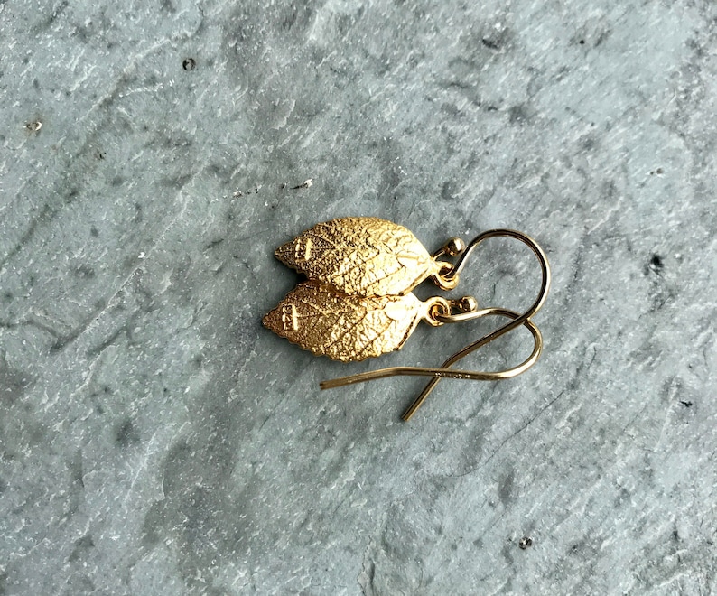 May include: A pair of gold leaf earrings with a delicate design. The earrings are made of gold-plated metal and have a simple, elegant look.