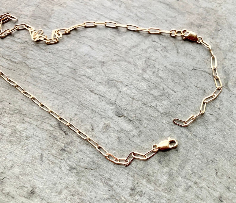 May include: A gold chain necklace with a lobster clasp closure. The chain is made of small, oval-shaped links.