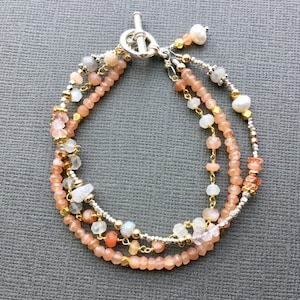 May include: A multi-strand bracelet with peach, white, and gold beads. The bracelet has a silver toggle clasp.