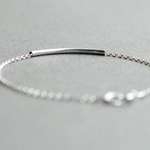 May include: A silver bracelet with a thin, straight bar charm. The bracelet is made of a delicate chain.