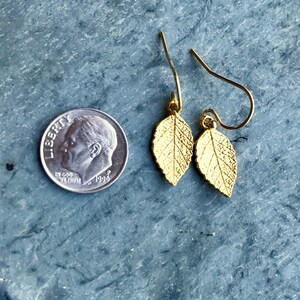 May include: A pair of gold leaf earrings with a delicate design. The earrings are small and dainty, and they would be perfect for a casual or formal occasion.