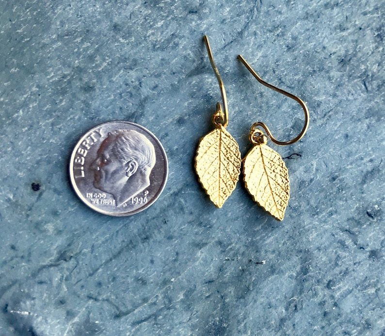 May include: A pair of gold leaf earrings with a delicate design. The earrings are small and dainty, and they would be perfect for a casual or formal occasion.