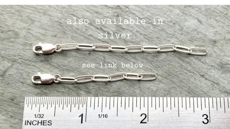 May include: Two silver chain links, each measuring approximately 1 inch in length, are laid out on a gray surface. A ruler is placed below the chains, with markings in inches. The text "also available in silver" and "see link below" are visible above the chains.