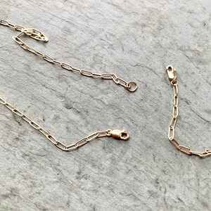 May include: Three gold chain links, each with a clasp, are laid out on a gray textured surface. The chains are made of small, oval-shaped links.