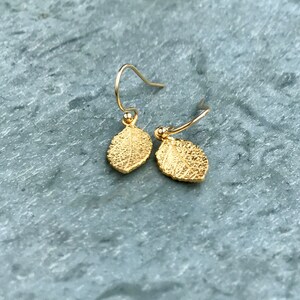 May include: A pair of gold leaf earrings with a delicate wire design. The leaves are textured and have a slightly hammered finish.