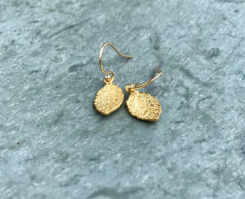 May include: A pair of gold leaf earrings with a delicate wire design. The leaves are textured and have a slightly hammered finish.