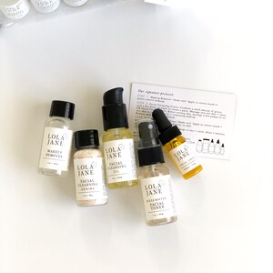 May include: A skincare essentials travel kit with several small bottles and jars. The bottles contain makeup remover, facial cleansing oil, facial cleansing grains, rosewater facial toner, and facial serum. The kit includes a clear travel bag and a card with instructions.