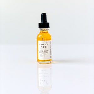Puede incluir: Una botella de vidrio transparente de suero facial Lola Jane con un cuentagotas negro. La botella contiene un l&iacute;quido de color dorado y tiene una etiqueta blanca con texto negro. La etiqueta dice "Facial Serum" y "Jojoba + Rosehip".