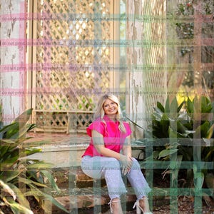 May include: A woman wearing a bright pink top and light blue jeans with pearl accents sits on a stone step. She is wearing white heels. The background includes a wooden gazebo and greenery.