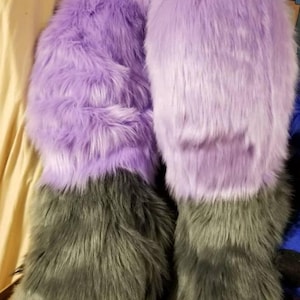 May include: Furry purple and gray costume legs. The upper portion is a vibrant purple, transitioning to a lighter shade, and the lower portion is a dark gray. The faux fur is long and fluffy, creating a soft, textured appearance. These legs are designed for cosplay or costume use.