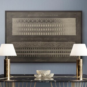 May include: A black marble table with a gold metal frame. The table has a geometric design with a series of vertical lines. Two lamps with white lampshades are on either side of the table. A vintage print of the Colosseum in Rome hangs on the wall behind the table.