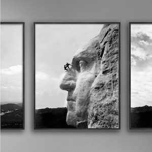 May include: A black and white photograph of Mount Rushmore National Memorial, showing the profile of George Washington's face. Two people are climbing the mountain, appearing small in comparison to the massive sculpture.