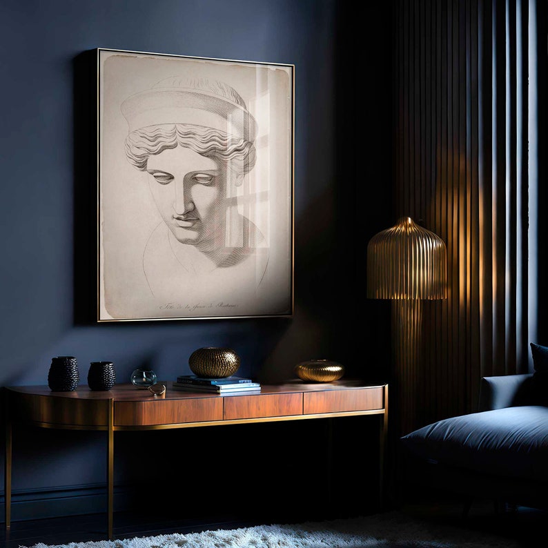 May include: A framed black and white print of a classical bust hangs on a dark blue wall. A wooden console table with gold accents holds decorative bowls. A gold-colored lamp with a ribbed shade stands nearby, illuminating the space.
